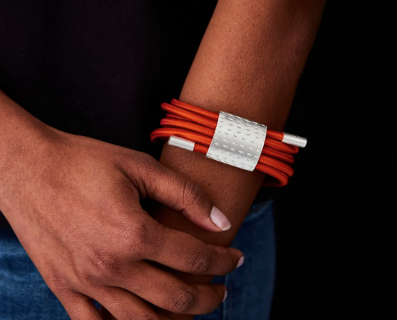 Close-up of a red cord bracelet with a silver textured centerpiece worn on the wrist.